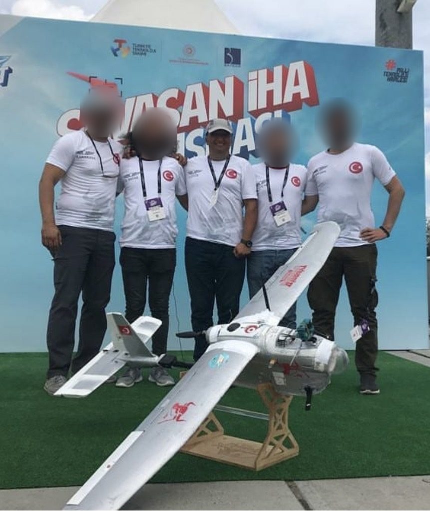 Teknofest Savaşan İHA Yarışması panosu önünde beş kişilik takım ve sabit kanatlı İHA; ortadaki Zafer
